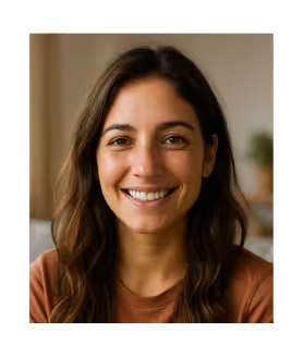 Mujer sonriente con cabello largo y oscuro, vistiendo una camiseta marrón, fondo interior desenfocado.
