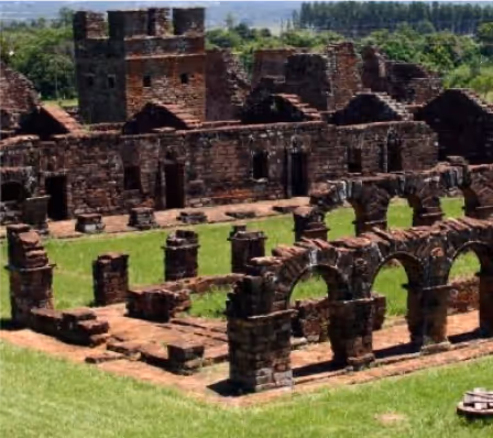 Ruinas antiguas de piedra con arcos y muros en un paisaje verde.